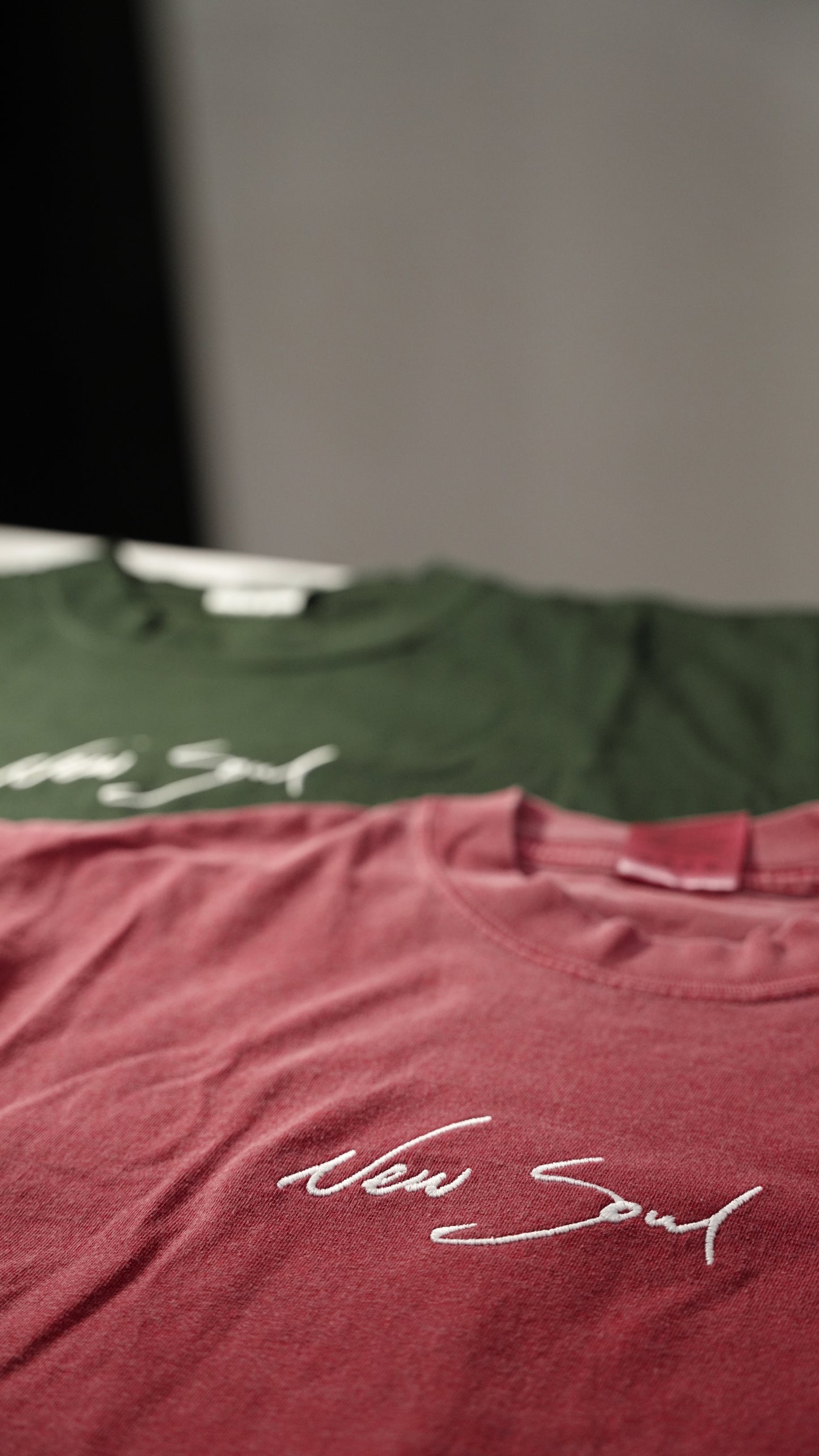 Two t-shirts, one green and one maroon, with 'New Soul' text on a blurred background.